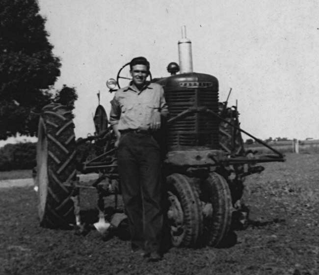 photo of J W Fiegenbaum standing beside a Farmall M tractor