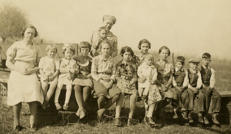 photograph of Henriette Fiegenbaum and 13 of her grandchildren sitting on a plank outside