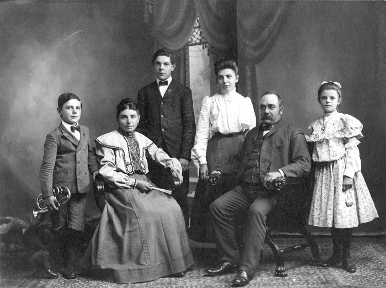 photographic studio portrait of the George L. and Charlotte E. (Etling) Gerber family.  The parents are seated in chairs and the children are standing around them.  The youngest, Louis August Gerber, is holding a brass horn.