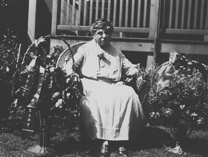 photograph of Charlotte Elisabetha (Etling) Gerber seated outside in a wicker chair with floral bouquets in baskets on either side of her chair